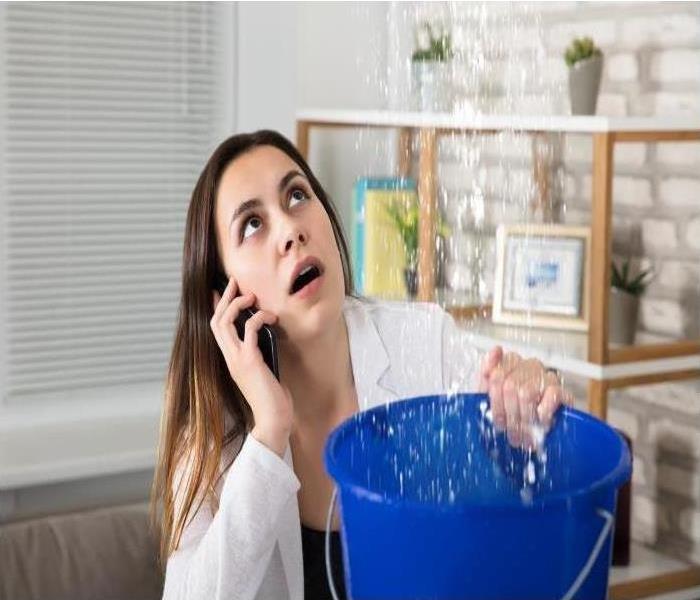 woman holding bucket collecting water entering home from ceiling