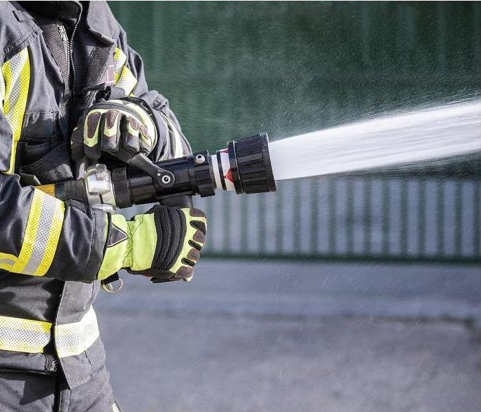 closeup of fireman's hand holding fire hose; water spraying from hose