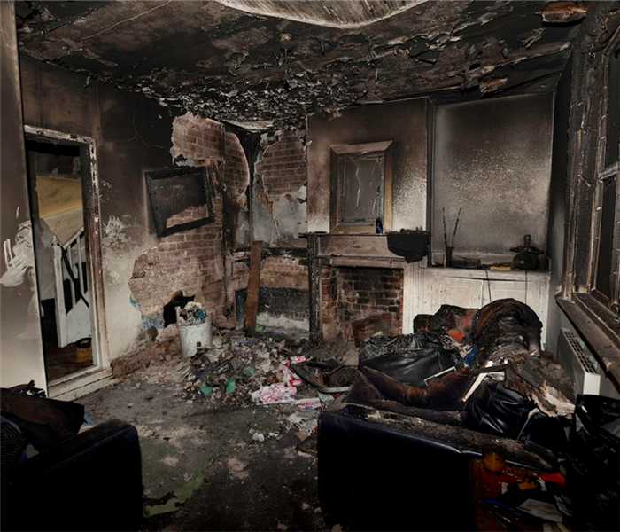 a fire damaged living room with debris on the floor and soot covering the walls