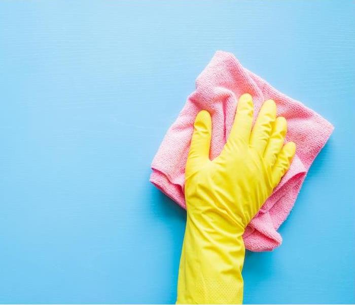 yellow gloved hand wiping a blue wall with a pink rag