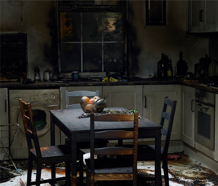a fire damaged kitchen with soot covering the counters and furniture and debris covering the floor